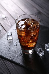 Photo of Sweet soda water in glass with ice cubes on black wooden table