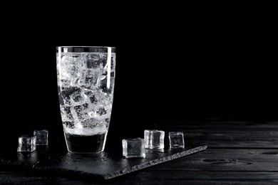 Refreshing soda water in glass with ice cubes on black wooden table, space for text