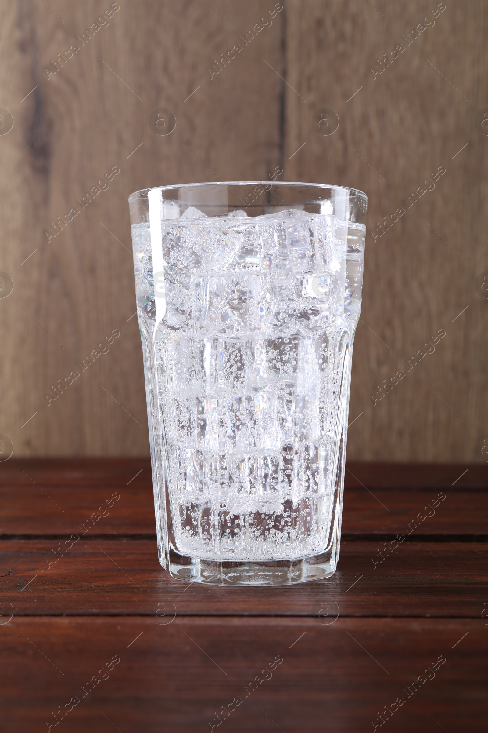 Photo of Refreshing soda water with ice cubes in glass on wooden table