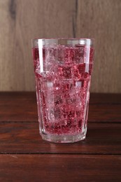 Photo of Sweet soda water with ice cubes in glass on wooden table