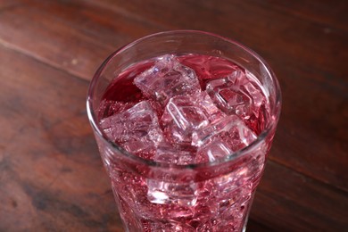 Photo of Sweet soda water with ice cubes in glass on wooden table, closeup