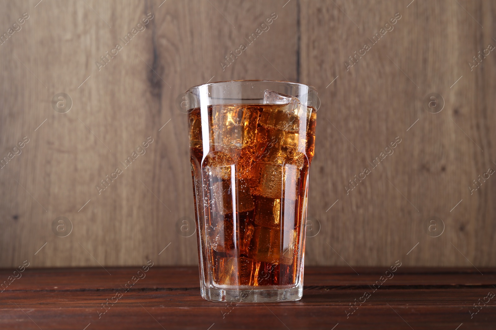 Photo of Sweet soda water with ice cubes in glass on wooden table