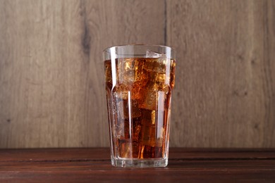 Photo of Sweet soda water with ice cubes in glass on wooden table