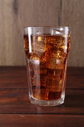 Photo of Sweet soda water with ice cubes in glass on wooden table, closeup