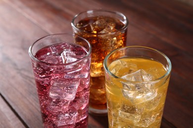 Photo of Refreshing soda water of different flavors with ice cubes in glasses on wooden table, closeup