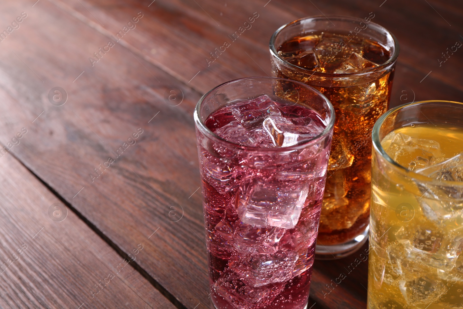 Photo of Refreshing soda water of different flavors with ice cubes in glasses on wooden table, closeup. Space for text