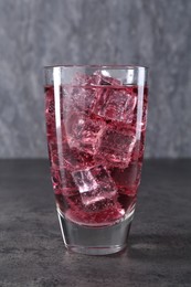 Photo of Sweet soda water with ice cubes in glass on grey table, closeup