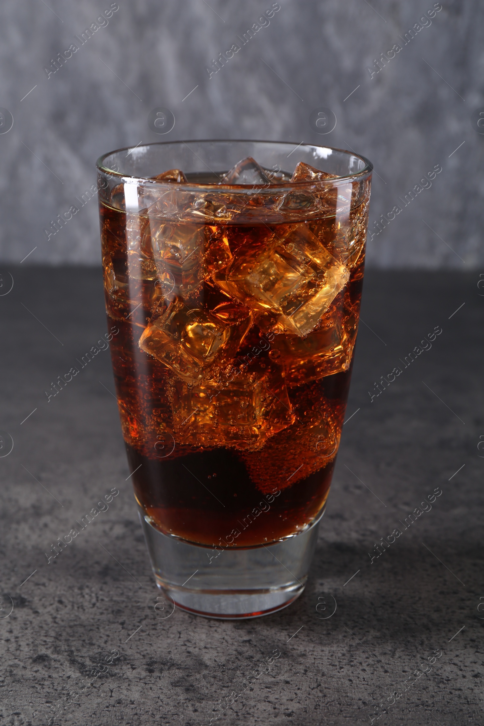 Photo of Sweet soda water with ice cubes in glass on grey table, closeup