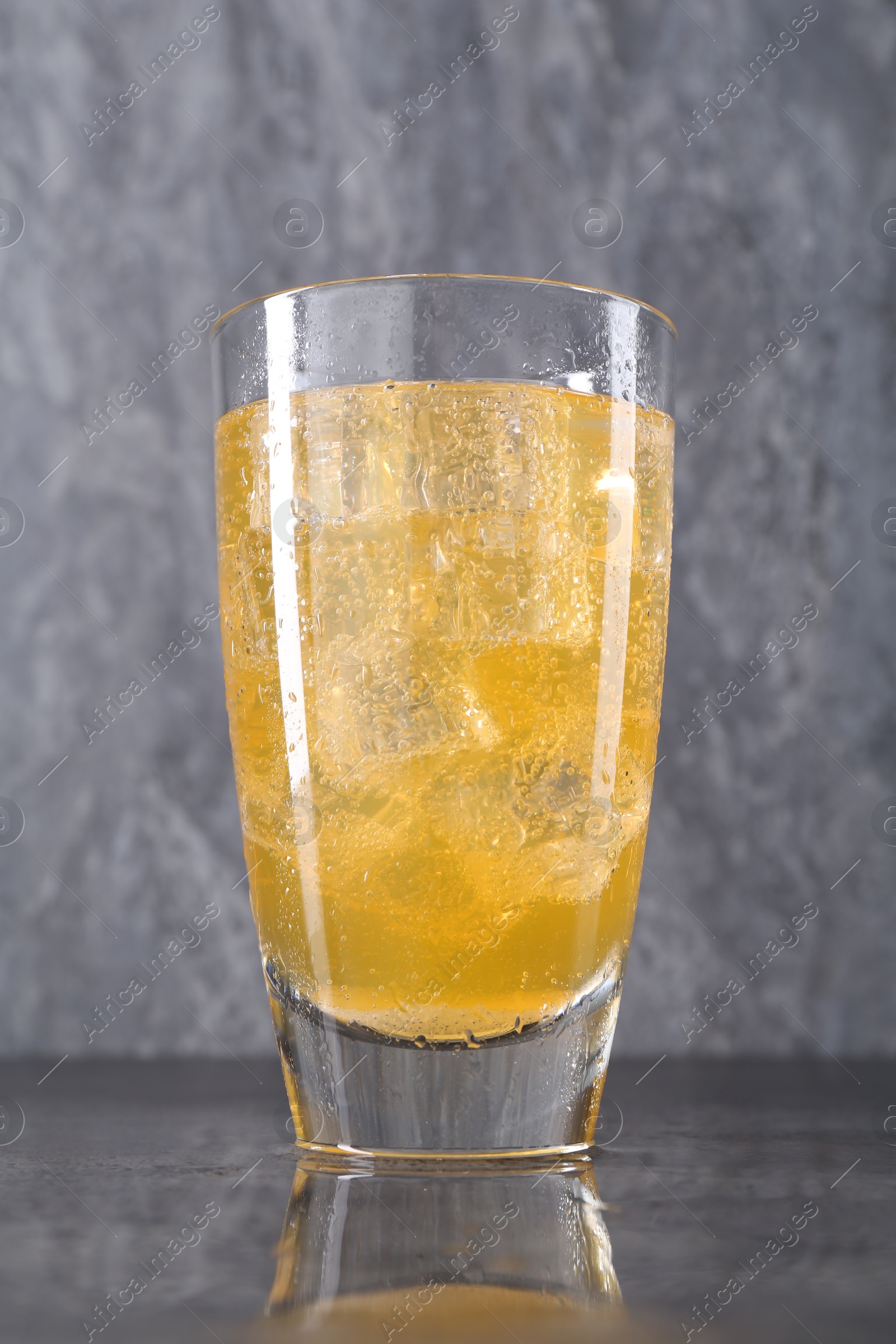 Photo of Sweet soda water with ice cubes in glass on grey table, closeup