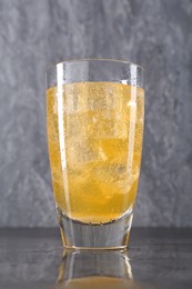 Photo of Sweet soda water with ice cubes in glass on grey table, closeup