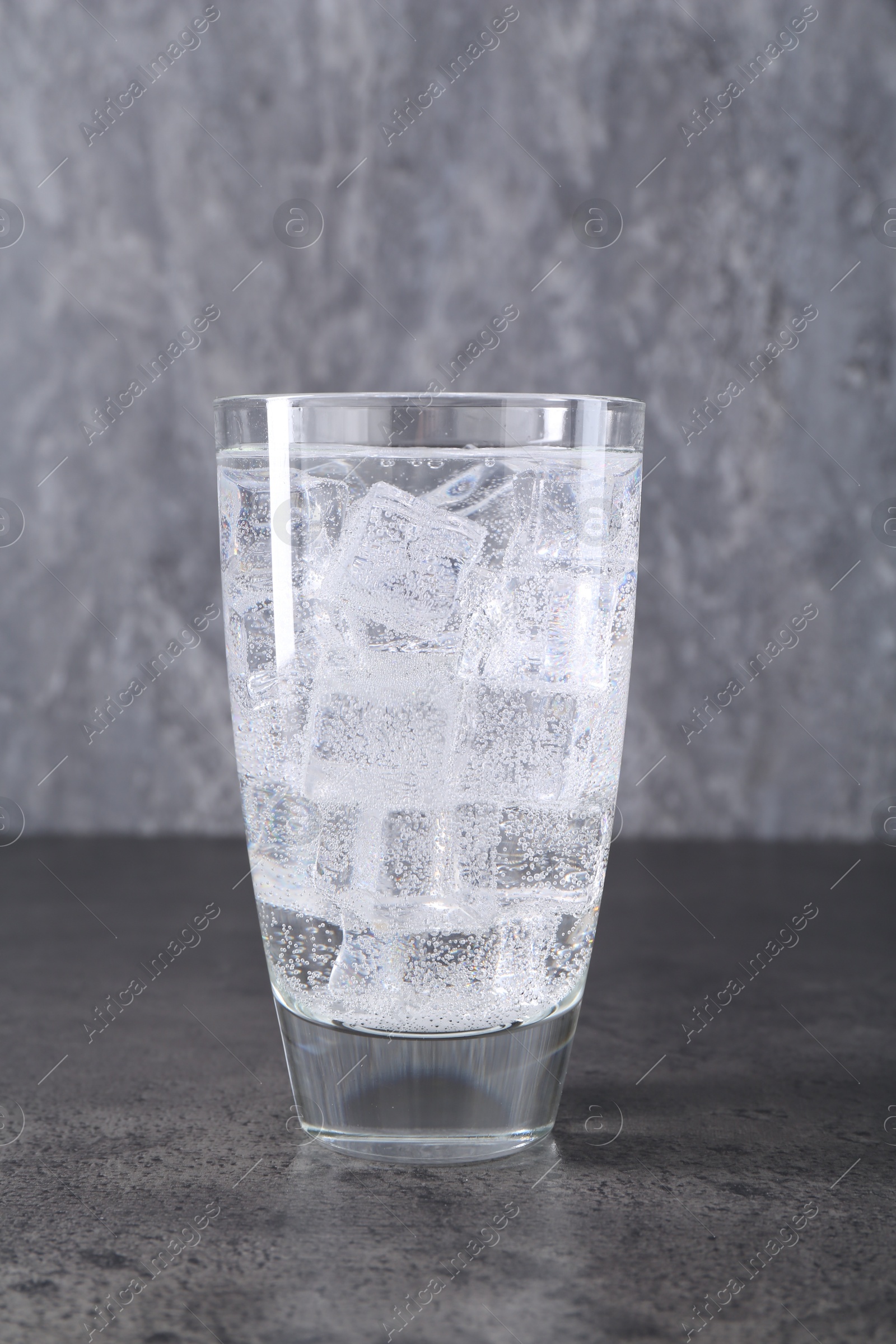 Photo of Refreshing soda water with ice cubes in glass on grey table