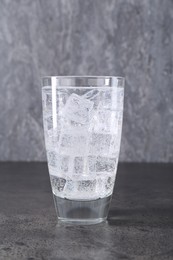 Photo of Refreshing soda water with ice cubes in glass on grey table