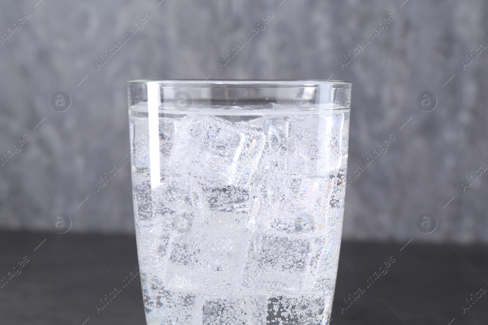 Photo of Refreshing soda water with ice cubes in glass on blurred background, closeup