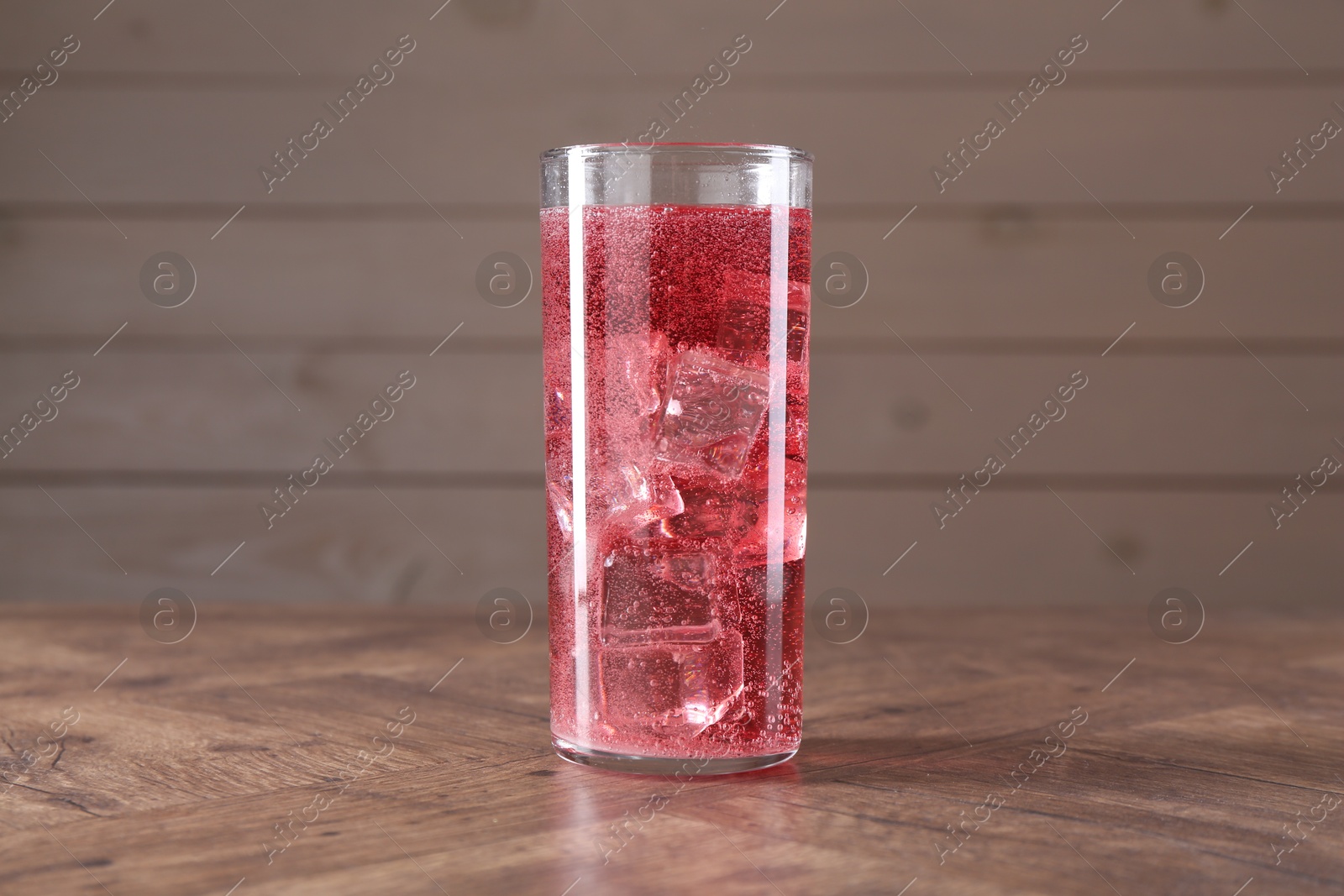 Photo of Sweet soda water with ice cubes in glass on wooden table