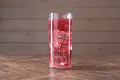 Photo of Sweet soda water with ice cubes in glass on wooden table