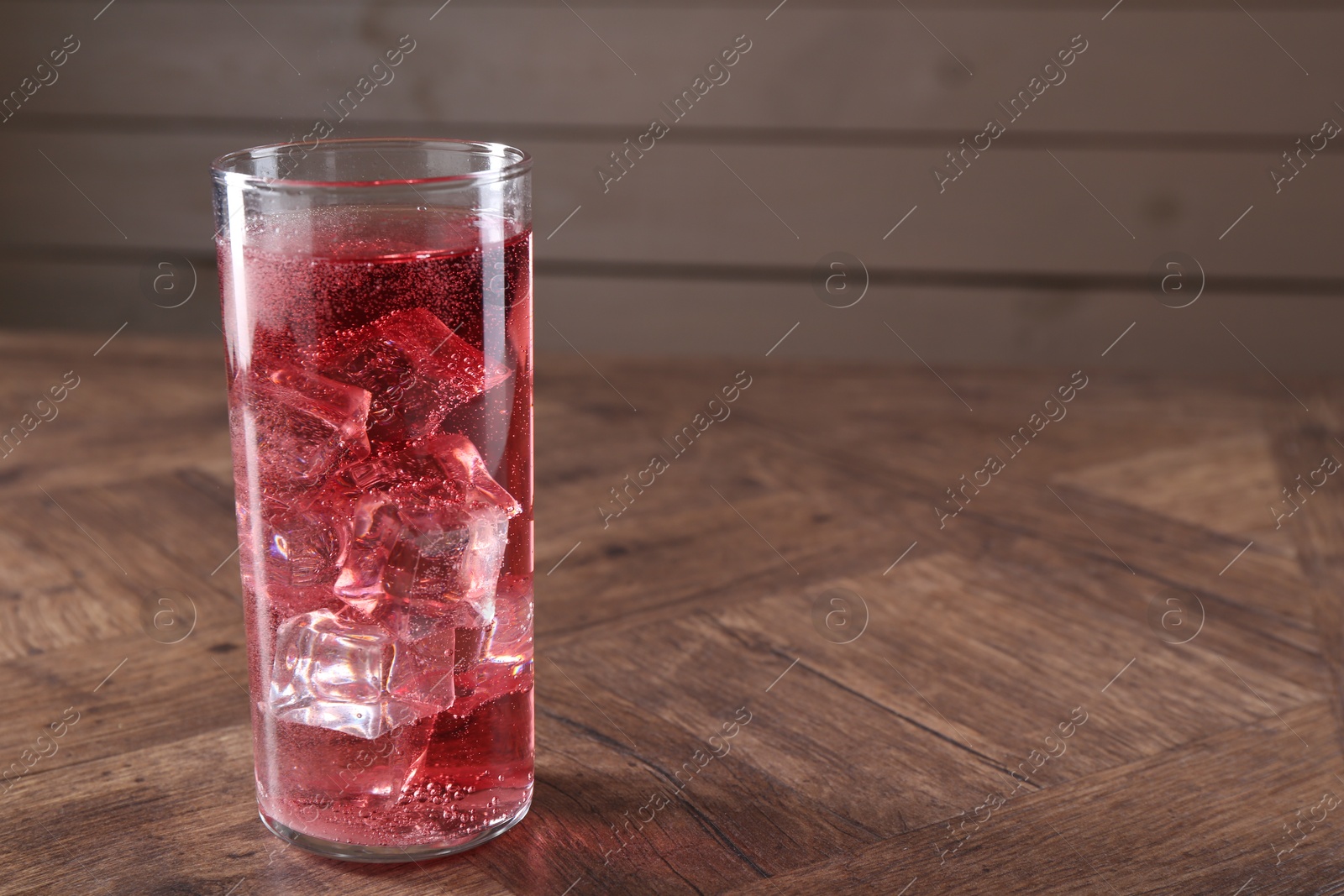 Photo of Sweet soda water with ice cubes in glass on wooden table, space for text