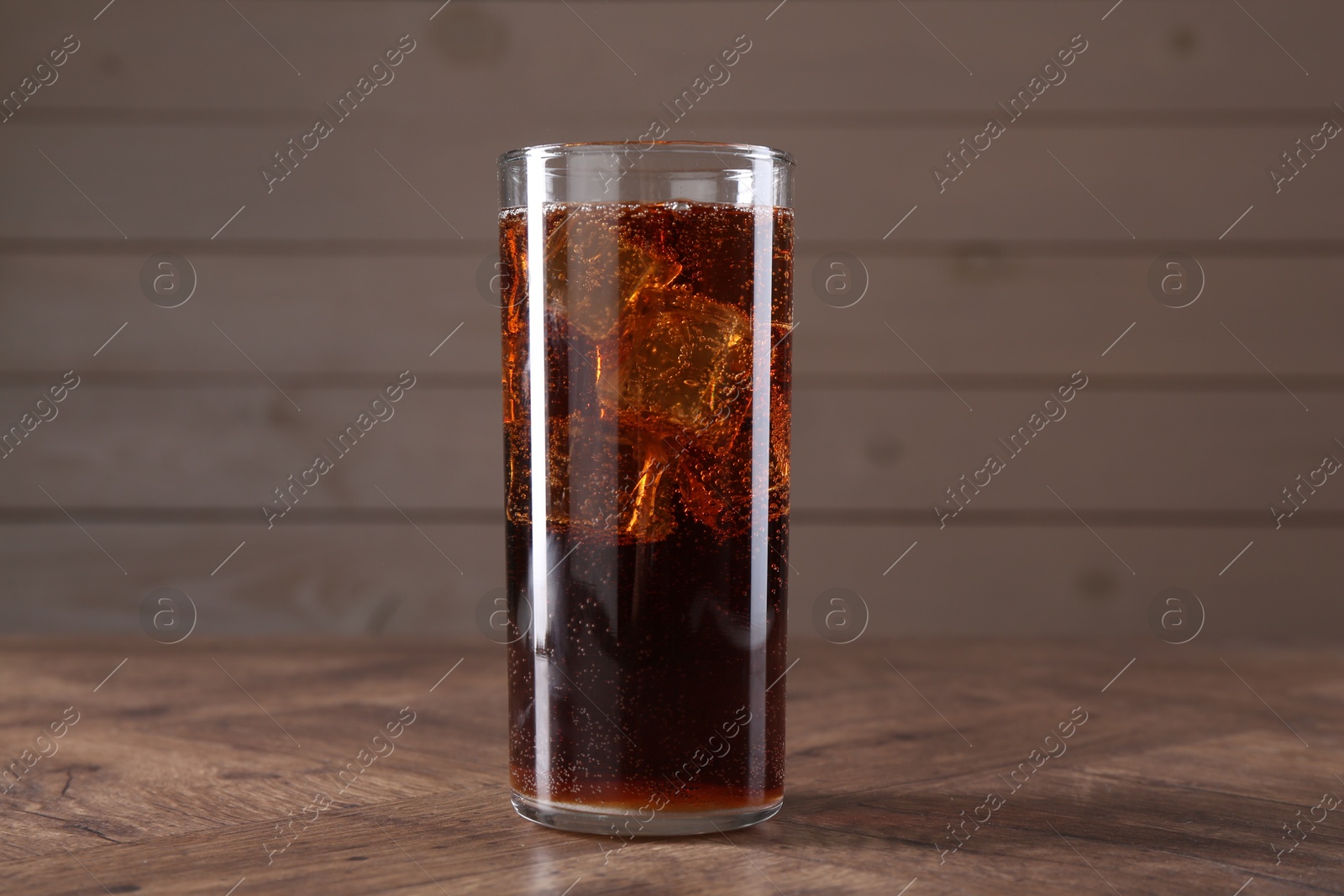 Photo of Sweet soda water with ice cubes in glass on wooden table