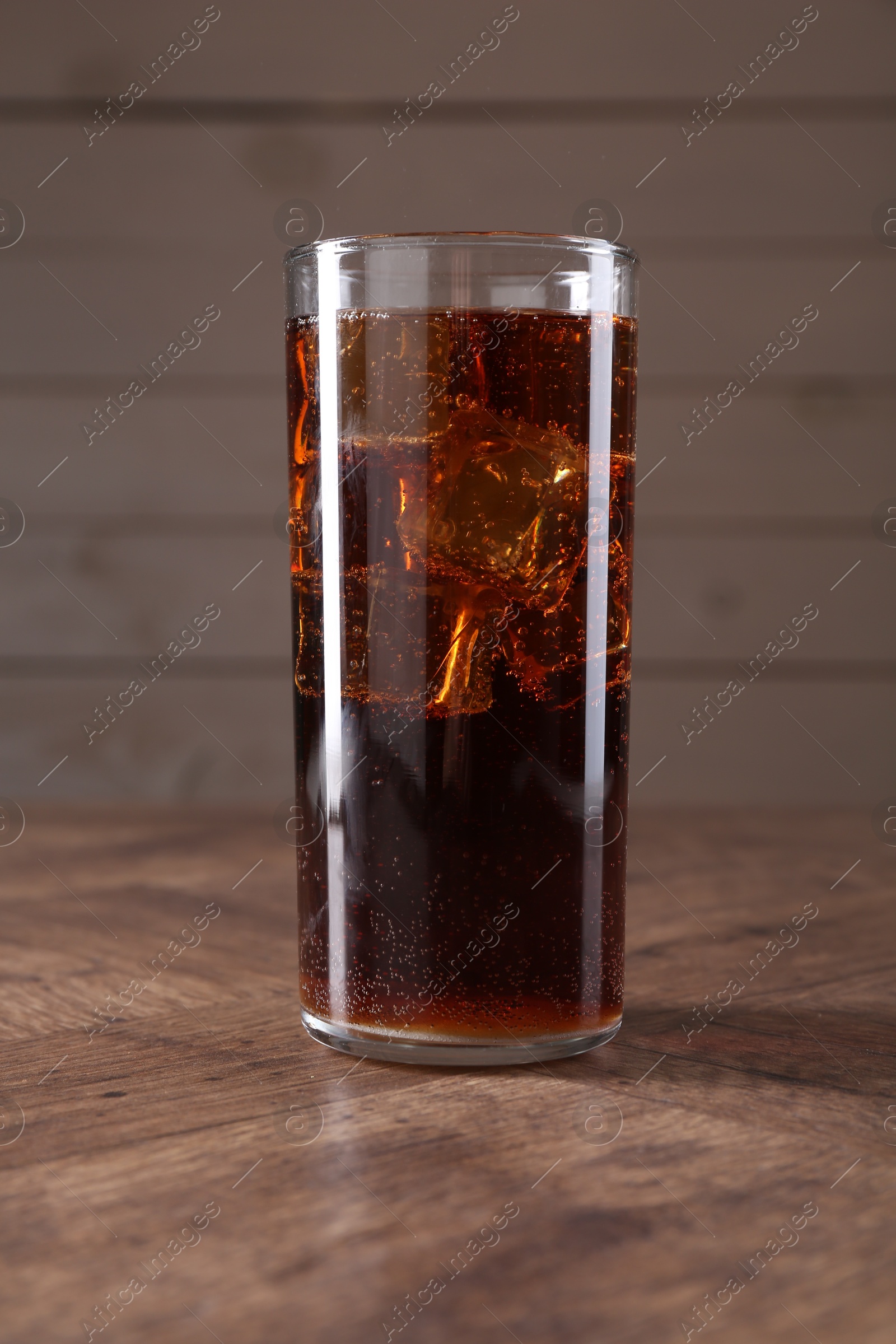 Photo of Sweet soda water with ice cubes in glass on wooden table, closeup