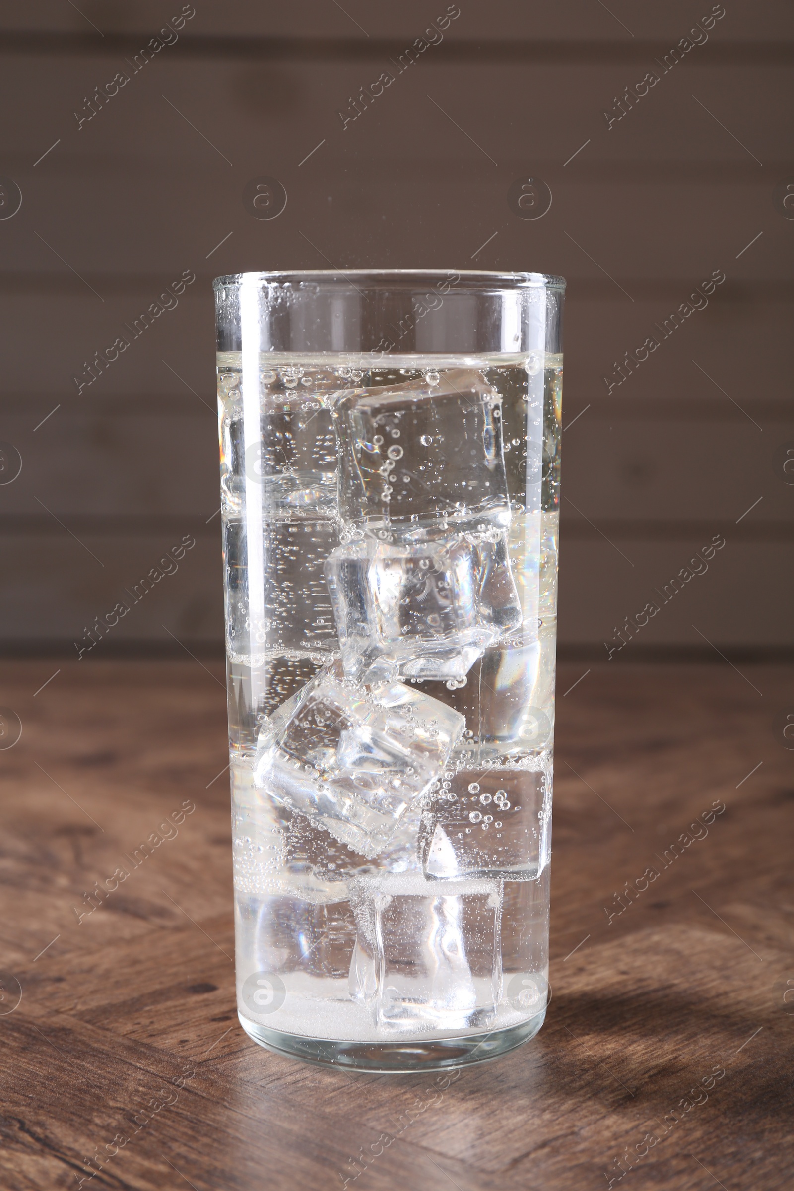 Photo of Refreshing soda water with ice cubes in glass on wooden table, closeup