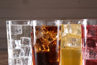 Photo of Refreshing soda water of different flavors with ice cubes in glasses on blurred background, closeup