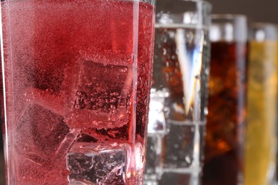 Photo of Refreshing soda water of different flavors with ice cubes in glasses, closeup