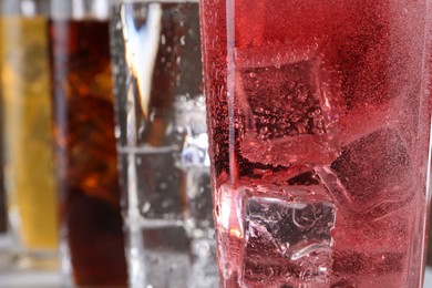 Photo of Refreshing soda water of different flavors with ice cubes in glasses, closeup