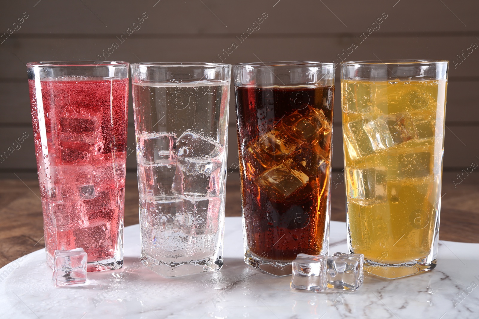 Photo of Refreshing soda water of different flavors in glasses with ice cubes on table