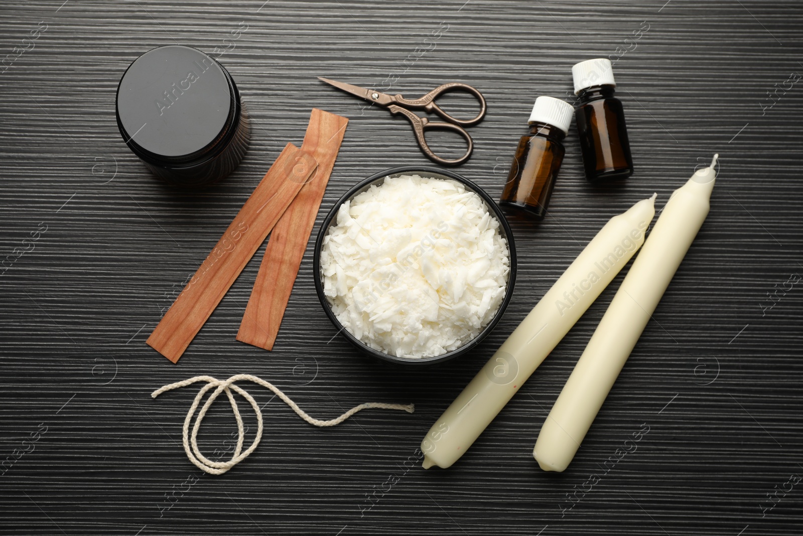 Photo of Soy wax, essential oils, twine, jar, wooden wicks and candles on black textured table, flat lay