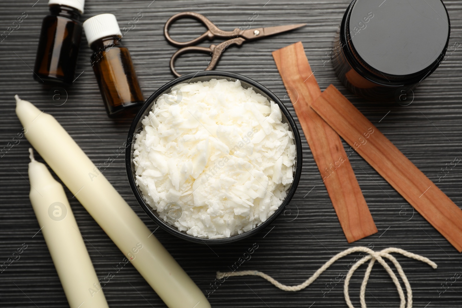 Photo of Soy wax, essential oils, twine, jar, wooden wicks and candles on black textured table, flat lay