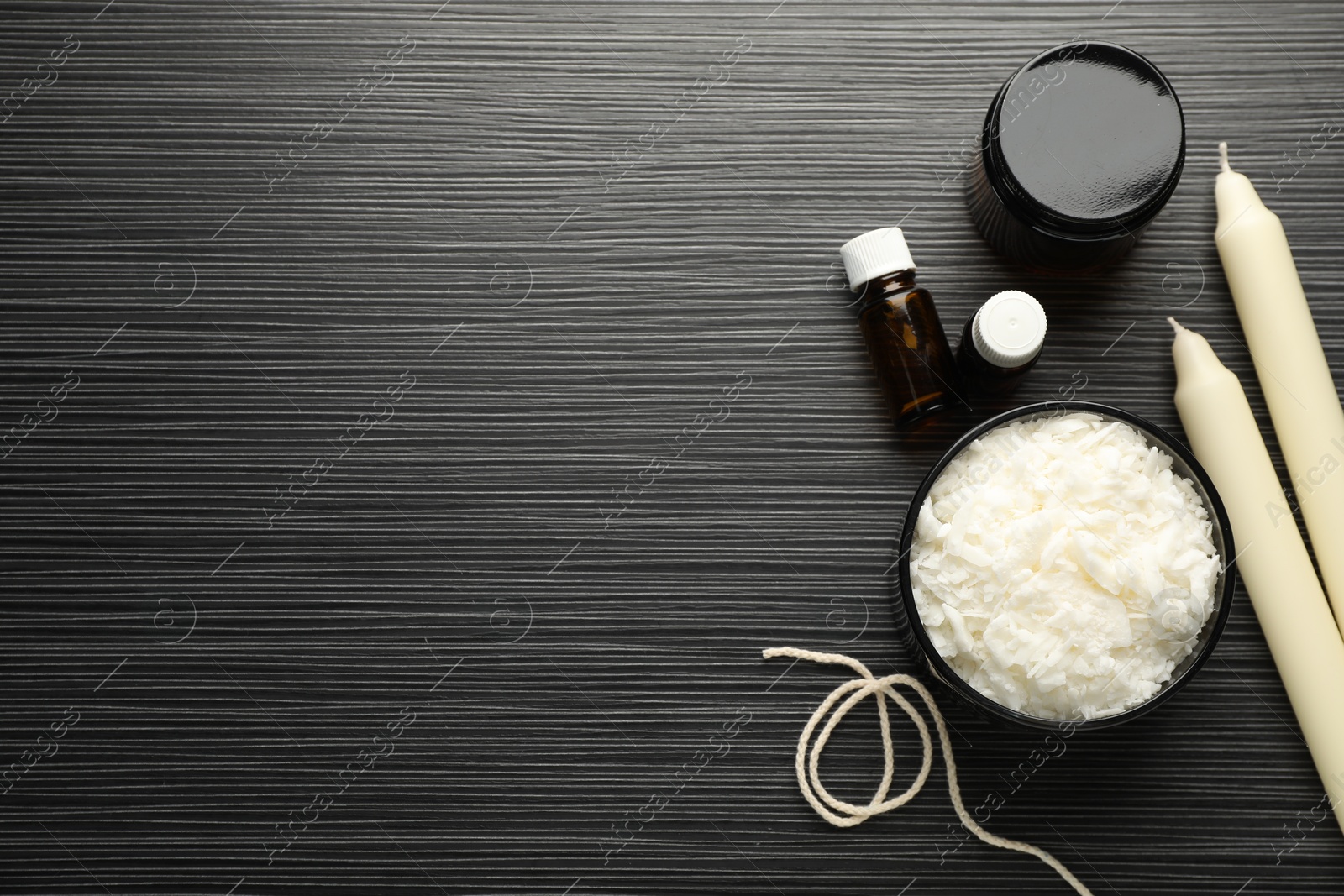 Photo of Soy wax, essential oils, twine, jar and candles on black textured table, flat lay. Space for text