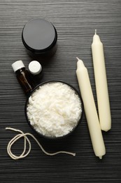 Photo of Soy wax, essential oils, twine, jar and candles on black textured table, flat lay