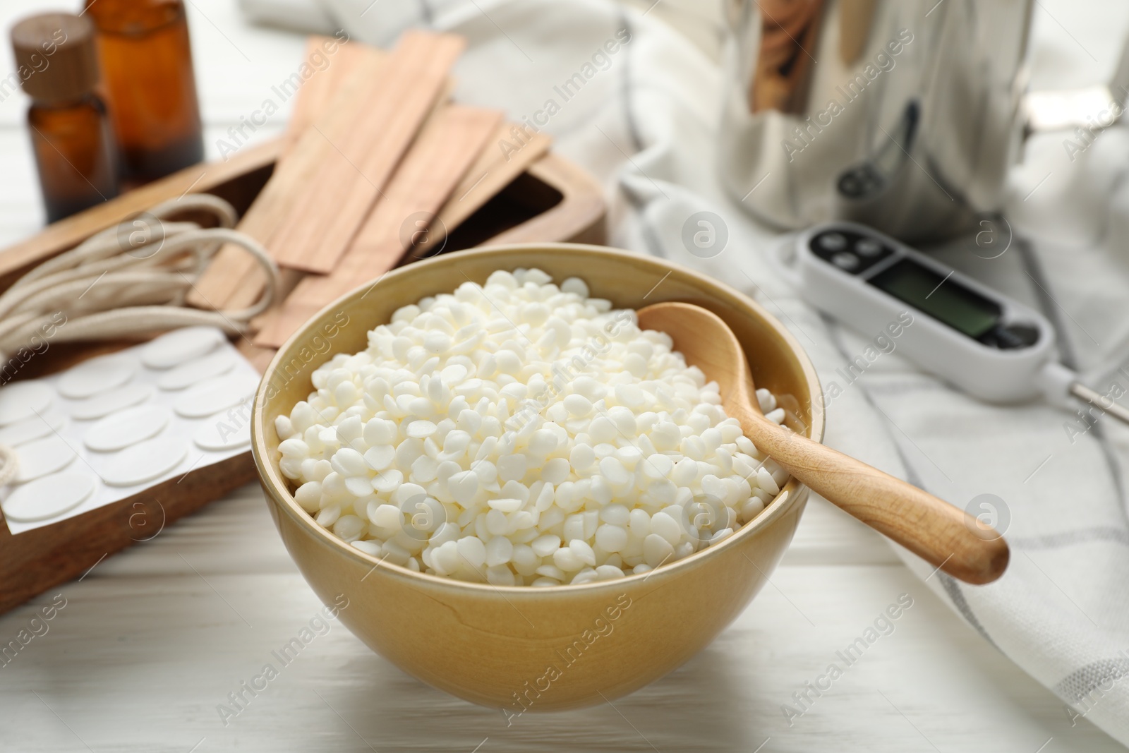 Photo of Soy wax in bowl and different tools for making candles on white wooden table, closeup