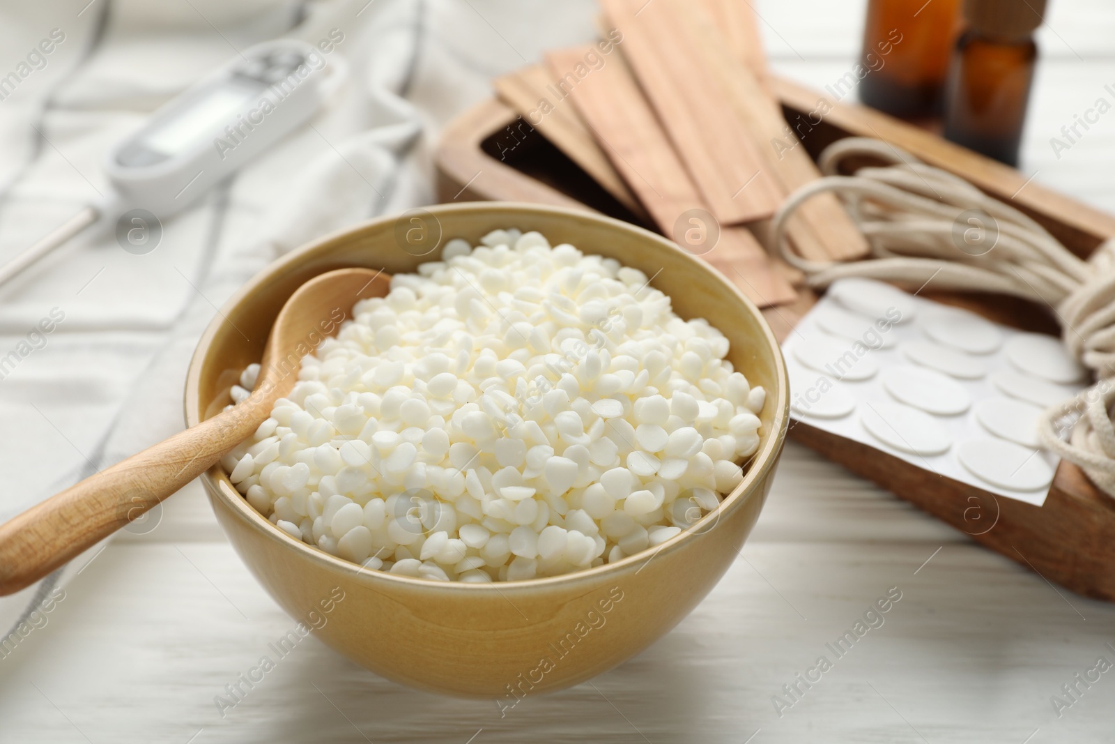 Photo of Soy wax in bowl and different tools for making candles on white wooden table, closeup