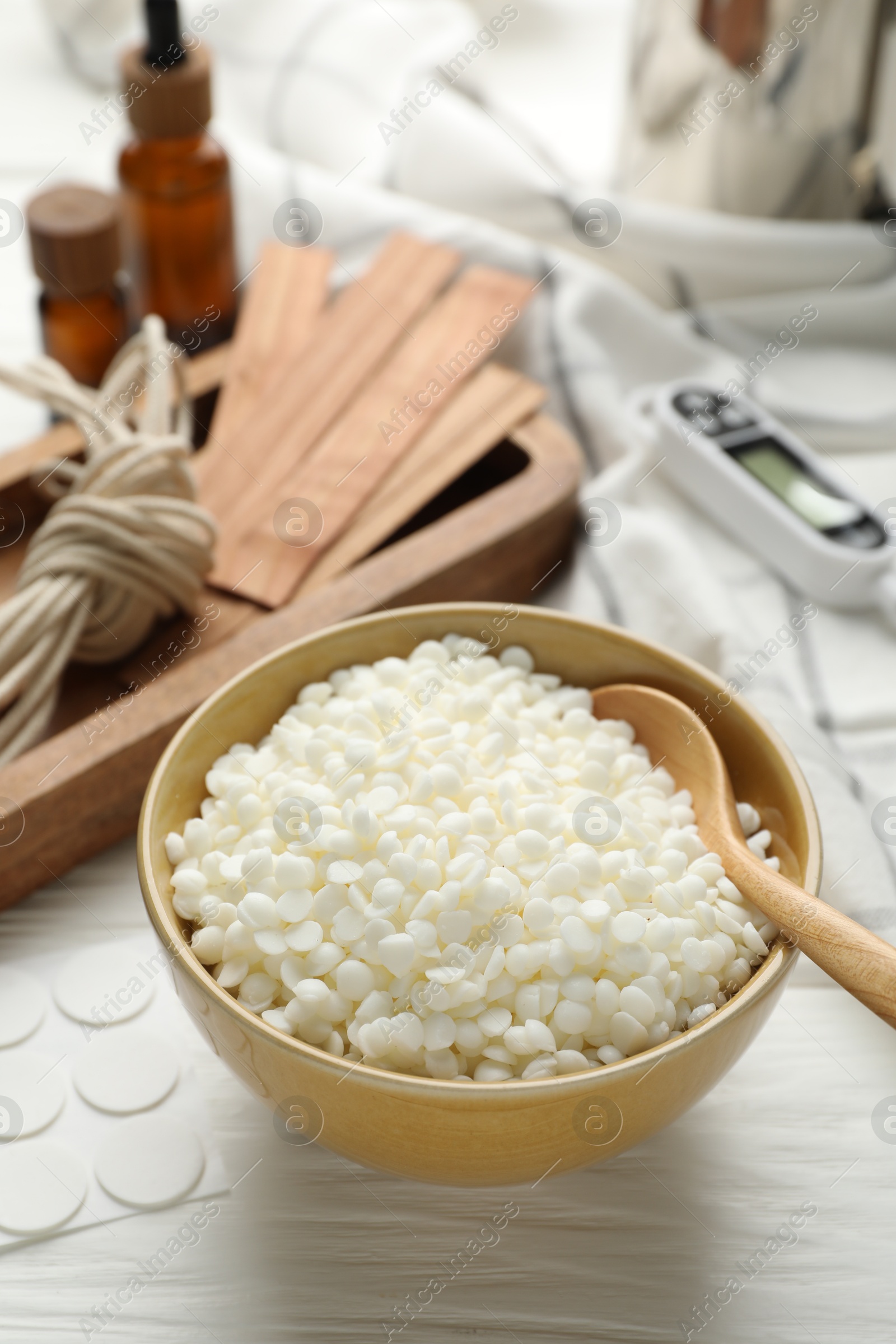 Photo of Soy wax in bowl and different tools for making candles on white wooden table, closeup