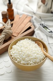 Soy wax in bowl and different tools for making candles on white wooden table, closeup