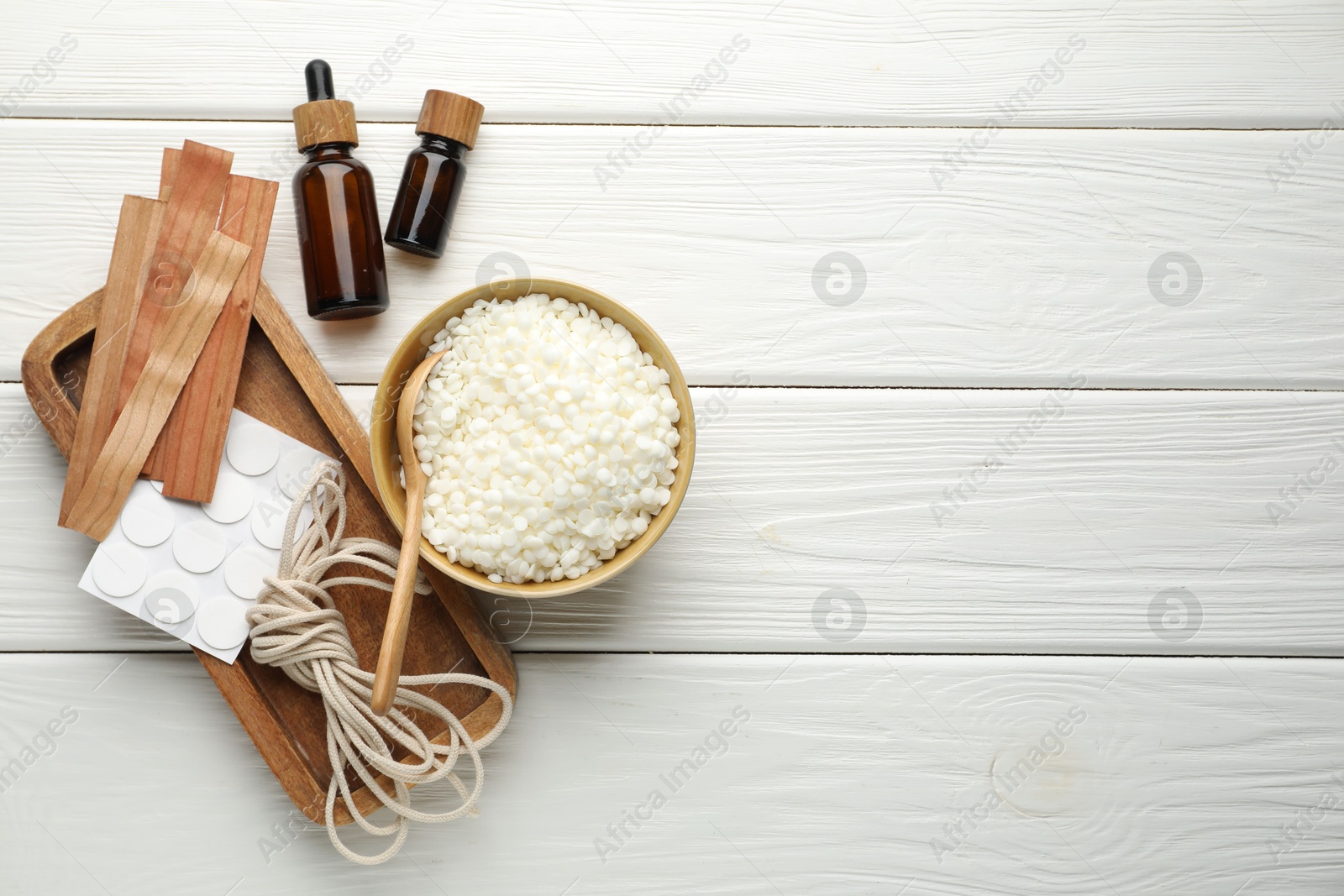 Photo of Making handmade candles. Soy wax in bowl, wicks, sticker and twine on white wooden table, flat lay. Space for text