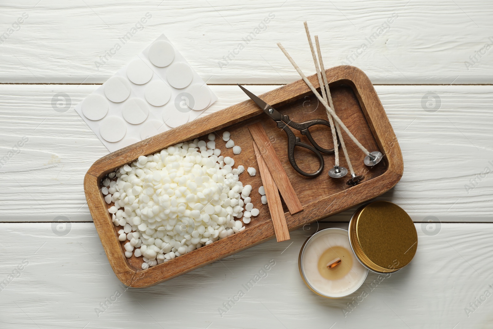 Photo of Soy wax, wicks, sticker, scissors and candle on white wooden table, flat lay