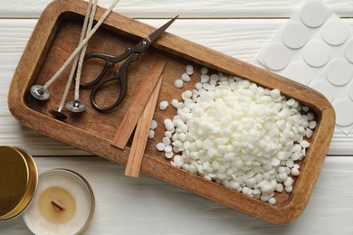 Photo of Soy wax, wicks, sticker, scissors and candle on white wooden table, flat lay