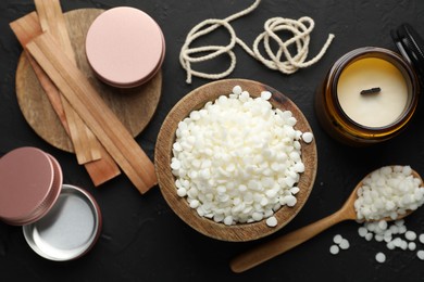 Photo of Soy wax in bowl, candle, wooden wicks, twine and jars on black table, flat lay