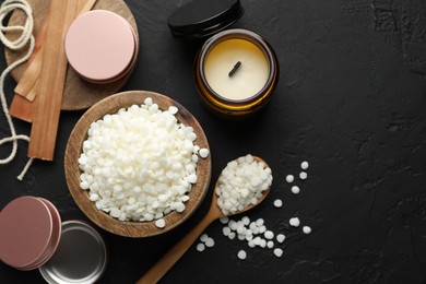 Photo of Soy wax in bowl, candle, wooden wicks, twine and jars on black table, flat lay. Space for text