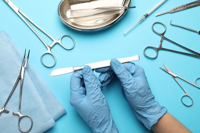 Photo of Doctor with different surgical tools on light blue background, top view