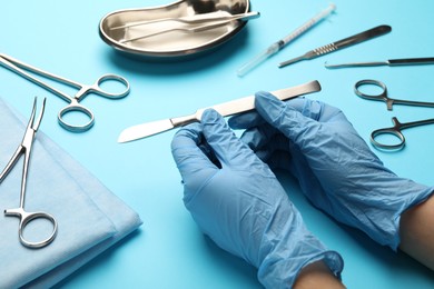 Photo of Doctor with different surgical tools on light blue background, closeup