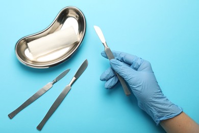 Photo of Doctor with surgical scalpels on light blue background, top view