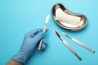 Photo of Doctor with surgical scalpels on light blue background, top view