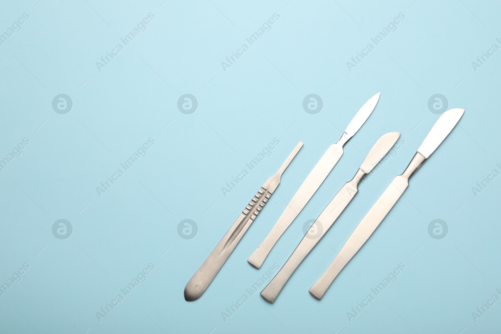 Photo of Different surgical scalpels on light blue background, flat lay. Space for text