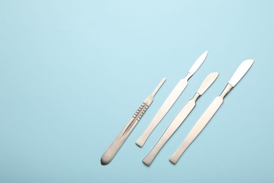 Photo of Different surgical scalpels on light blue background, flat lay. Space for text