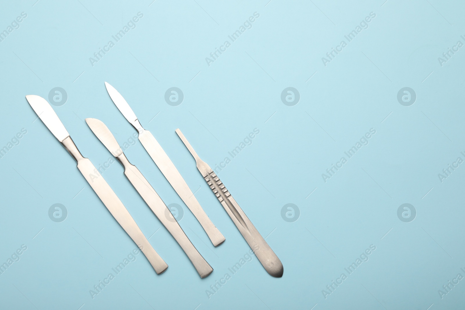 Photo of Different surgical scalpels on light blue background, flat lay. Space for text