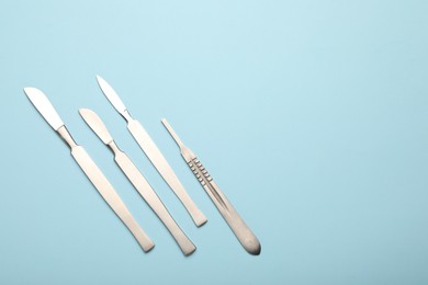 Photo of Different surgical scalpels on light blue background, flat lay. Space for text