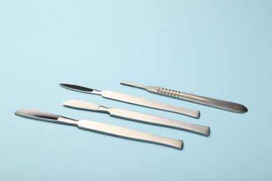 Photo of Different surgical scalpels on light blue background, closeup