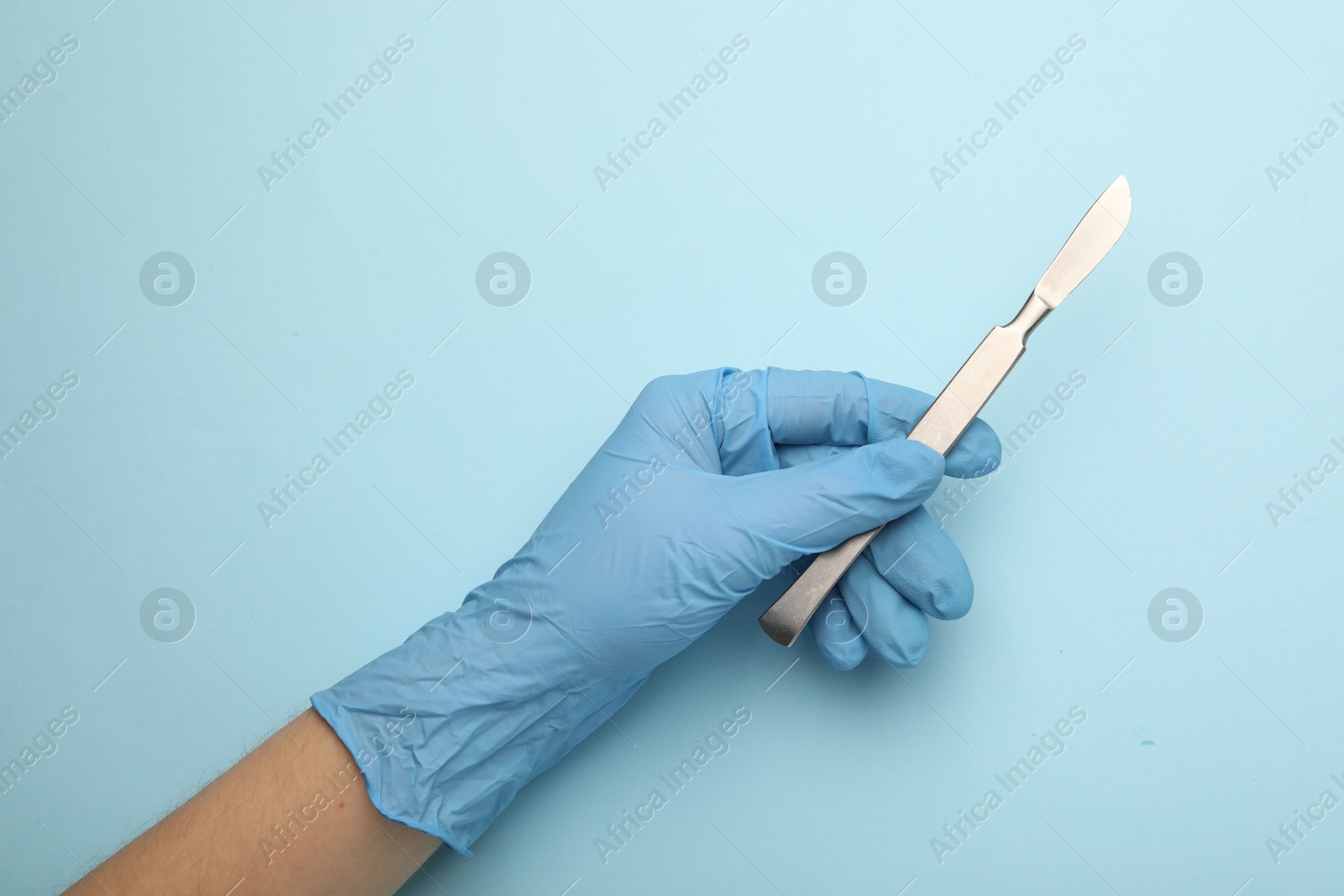 Photo of Doctor with surgical scalpel on light blue background, top view. Space for text